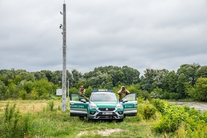 Funkcjonariusze SG podczas patrolu przy rzece granicznej Bug, w tle maszt bariery elektronicznej.