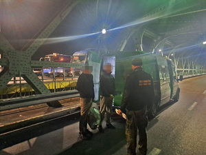 Funkcjonariusze SG podczas doprowadzenia osób zatrzymanych przy pojeździe służbowym