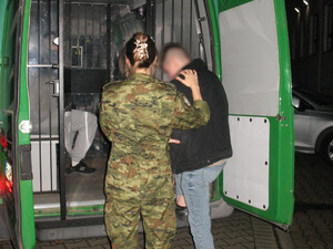 Funkcjonariusze SG podczas doprowadzenia osób zatrzymanych przy pojeździe służbowym